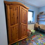 Ein Zimmer mit Holzschrank, Schreibtisch, Stühlen und Spielteppich.