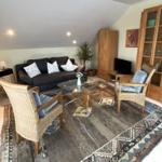 Wohnzimmer mit Sofa, zwei Sesseln und Glas-Tisch auf Teppich.