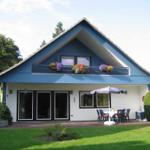 Ein Haus mit blauem Dach und Balkon, Gartenbereich mit Tisch und Sonnenschirm.