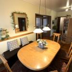 Esszimmer mit Holztisch, Stühlen und Wandspiegel. Bücherregal und Blumenvase sind sichtbar.