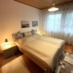 Schlafzimmer mit Bett, Nachttisch und Fenster mit Vorhängen.