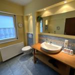 Badezimmer mit Waschbecken, Toilette und Badewanne. Fenster mit Vorhängen.