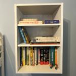 Weißer Bücherregal mit drei Etagen und Büchern sowie zwei Figuren.