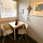 Kleiner Raum mit Tisch, zwei Stühlen und Fenster. Wandbild und Spielzeug sind sichtbar.