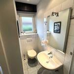 Badezimmer mit Waschbecken, Spiegel, Toilette und Fenster