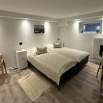 Schlafzimmer mit Bett, Nachttisch, Stuhl und Schreibtisch. Holzboden und Fenster.