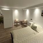 Schlafzimmer mit Bett, zwei Stühlen und Wandbild. Holzfußboden und weiße Wände.