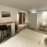 Schlafzimmer mit Schreibtisch, Stuhl und Bett. Hintergrund: Kleine Sitzgelegenheit und Schrank.