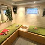 Zwei grüne Matratzen auf Holzrahmen, Wandspiegel, Pflanze, Fenster und Bild.