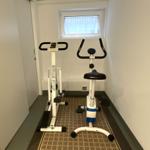 Fitnessraum mit Stepper und Fahrradtrainer unter einem Fenster