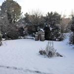 Schneebedeckter Garten mit Steinbau und Sträuchern.