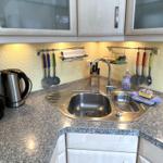 Küche mit Spüle, Kochutensilien und Kaffeemaschine auf Arbeitsfläche.