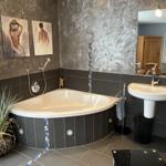 Bad mit Whirlpool, Waschbecken und Spiegel. Wandgestaltung und Pflanze sichtbar.