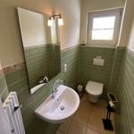 Badezimmer mit Waschbecken, Spiegel, Toilette und Fenster.