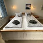 Schlafzimmer mit Doppelbett, zwei Nachttischen und Fenster mit Segelbootmodell.