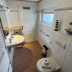 Badezimmer mit Toilette, Waschbecken und Fenster. Dekoration: Leuchtturm und Segelschiffmodell.