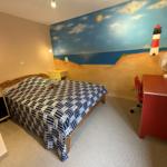 Schlafzimmer mit Strand-Malerei, Bett, Schreibtisch und Ventilator.