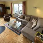 Wohnzimmer mit Sofa, Sessel und Glas-Tisch auf Parkettboden.