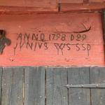 Holztor mit roter Tafel, auf der ANNO 1798 D29 und ein Kreuz eingraviert sind.