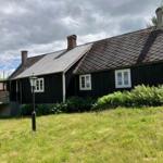 Schwarzes Holzhaus mit weißen Fenstern und Dachgauben im Grünen.