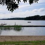Strand mit Bootssteg und ruhigem See im Hintergrund.