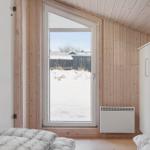 Bedroom with wooden walls, window, and bed. Outside snow and fence.