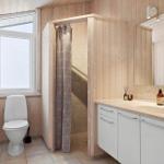 Bathroom with toilet, shower, and sink. Wooden walls and window.