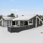 Black wooden house with snow, large window area, and white car in front.