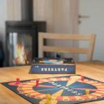 A board game on a wooden table in front of a fireplace with burning fire.
