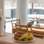 Fruit bowl and lit candles on kitchen island, dining area in background with snowy view.