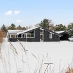 Black house with snow, white car, and trees in the background.