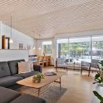 Living and dining area with sofa, table, and chairs. Large windows and wooden ceiling.
