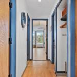 Hallway with hardwood flooring and blue door frames. Walk-in closet and view into living area.
