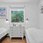 Two beds, dresser, and window with view of forest.