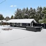 Black house with snow-covered roof and terrace among trees.