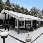 Black house with snow-covered roof and patio in the woods