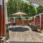 Deck with table, chairs, and umbrella. Red wooden fence and plants.