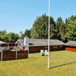 Red wooden house with terrace, garden, and lounge chairs. Background: dense trees.