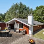 Red vacation house with terrace, grill, and lawn area in green surroundings.