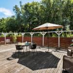 Terrace with table, chairs, and umbrella. Surrounded by forest and wooden railing.