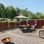 Terrace with seating, umbrella, and fire pit. Surrounded by wooden fence and trees.