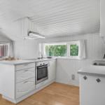 Kitchen with white cabinets, wooden floor, and windows overlooking greenery.