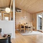 Wood-paneled kitchen with dining table, chairs, and windows. Wood-burning stove and seating area in foreground.