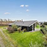 Modern wooden cabin with terrace and garden. Green lawn and sky in the background.