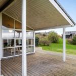 Deck with wooden flooring and glass walls. View of green lawn and trees.