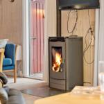 Kaminofen mit brennendem Feuer in einem Raum mit Holzwänden und blauer Couch.