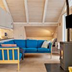 Wohnbereich mit blauem Sofa, Kamin und TV. Holzwände und -decke.