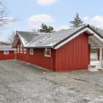 Rotes Holzhaus mit grauem Dach und Veranda auf Kiesfläche.