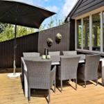 Terrace with table, six chairs, and sun umbrella. Wooden deck and dark fence.