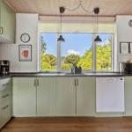 Kitchen with green cabinets, window with view of greenery, sink and dishwasher.